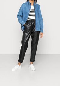 Chemise en denim à boutons portée par-dessus un débardeur noir à rayures, associée à un pantalon en cuir noir et des baskets blanches. Textures douces et design décontracté.