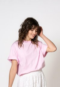 Rosa bomulls T-skjorte med avslappet passform og rullede ermer, kombinert med et hvitt blonderet skjørt. Enkel design, uten synlige mønstre eller grafikk.