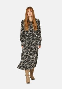Vestido negro con estampado floral, de manga larga, con cierre de botones y cintura ceñida. Tejido suave con intrincados patrones de flores. Combinado con botas beige hasta la rodilla.