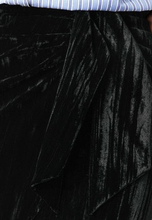 Jupe en velours noir avec une finition texturée, présentant un design drapé à la taille et une apparence lisse et brillante.