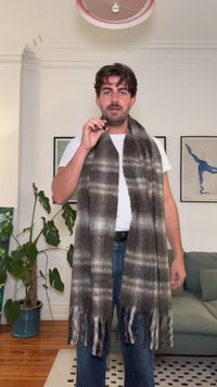 Grå og hvit rutete skjerf med frynser, laget av et mykt materiale, båret drapert rundt halsen, kombinert med en hvit T-skjorte og blå jeans.