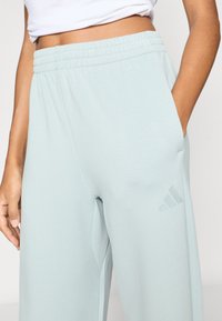 Ljusblå atletiska joggingbyxor i mjukt tyg. Har elastisk midja, sidofickor och en subtil logga på vänster ben.