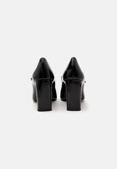 Paire de chaussures à talons hauts en cuir verni noir avec un dos arrondi fermé et des talons épais, vues de dos sur fond blanc.