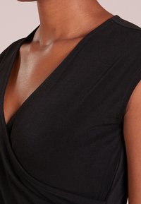 Svart topp med djup V-ringning, korta ärmar och en slät textur. Tyget faller elegant med subtila sömdetaljer.