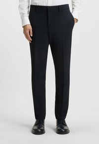Tailored dark navy trousers in lightweight fabric with pleats, side pockets, and a sleek fit, paired with black formal shoes.