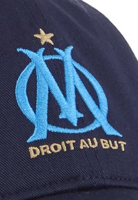 Gorra de béisbol azul marino con un logo bordado en azul claro con la "M" y una estrella dorada, con el texto "DROIT AU BUT" en dorado debajo.