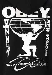 Schwarzer Hoodie mit auffälligen weißen Grafiken. Das zentrale Design zeigt eine Figur, die einen Globus hebt, umgeben von den Texten "OBEY" und "NEW VISIONS".
