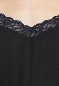 Černý top na ramínka s krajkovým výstřihem ve tvaru vlny, jemnou texturou látky a rovným střihem. Minimalistický bez dalších ozdob.
