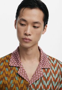 Short-sleeve shirt with a brown, turquoise, and orange zigzag pattern; pink geometric collar; textured fabric.