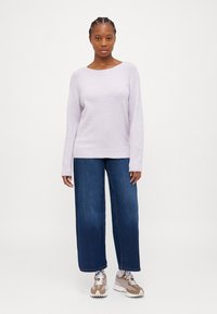 Sweater de malha lilás claro com mangas longas e um decote amplo, combinado com jeans azuis largos e ténis bege.