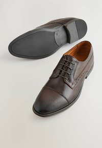 Zapatos de vestir de cuero marrón con puntera perforada, cordones planos y suela de goma texturizada. Diseño clásico con sutiles acentos de costura.