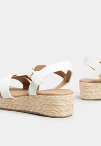 Sandali piattaforma bianchi con base in juta intrecciata, dotati di cinture incrociate e dettaglio con fibbia. Soletta liscia con una texture naturale.