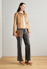 Smeđa antilop cropped jakna s dugmadi na pritisak, uparena sa sivim širokim trapericama i tamnim platformama. Model drži smeđi clutch.