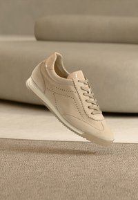 Μπεζ αθλητικό παπούτσι από λείο σουέντ με διάτρητο σχέδιο, στρογγυλεμένη μύτη και επίπεδη σόλα από καουτσούκ. Διαθέτει κορδόνια και ραφές σε αντίθετο χρώμα.