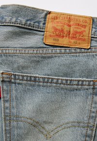 Ljusblå denimjeans med en beige läderlapp som har "Levi Strauss & Co." och en röd etikett. Har orange sömnad och klassisk bakfickdesign.