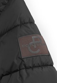 Czarna kurtka puchowa z teksturowaną brązową łatą na ramieniu, na której znajduje się wytłoczone logo "POLO CLUB" w okrągłym wzorze.