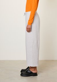 Lichtgrijze joggingbroek met een taillekoord, voorzien van een losse pasvorm en rechte pijpen. Gecombineerd met een oranje longsleeve en zwarte klompen.