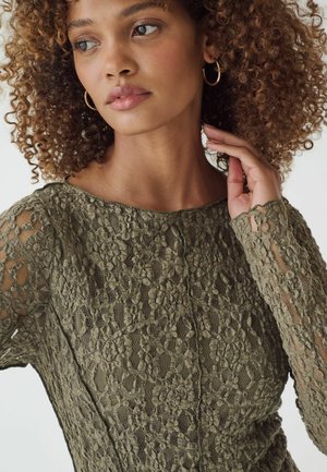 Olivengroene kanttop met bloemenpatronen, lange mouwen en een ronde halslijn, met een gestructureerde stof en doorschijnende accenten.