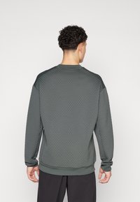 Pull en sergé vert foncé avec un motif en nid d'abeille, manches raglan, col et poignets côtelés. Tissu lisse et coupe décontractée.