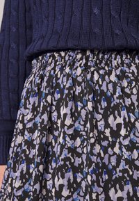 Floral-patterned skirt with a black base, featuring blue and lavender accents. Elastic waistband and pleated texture, paired with a navy cable-knit sweater.