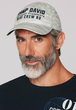 Gray cap with "CAMP DAVID" and "BLUE CREW 63" embroidered in blue. Textured fabric, curved brim. Dark t-shirt with graphic design underneath.