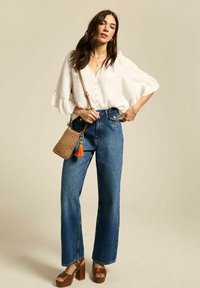 Witte, knoopsluiting blouse met gerimpelde mouwen, gecombineerd met hoge taille, rechte spijkerbroek in blauw en bruine plateausandalen. Inclusief geweven handtas.