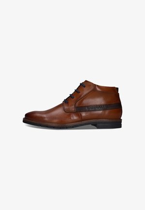 Brauner Leder-Herren-Knöchelstiefel mit schwarzen Schnürsenkeln und einem schwarz vernähten Streifendetail über der Sohle auf weißem Hintergrund.