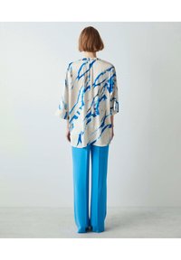 Blusa ampia di colore crema con righe blu, abbinata a pantaloni a gamba larga di un blu vivace; entrambi realizzati in materiali leggeri.