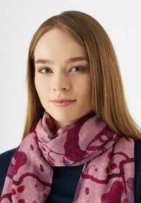 Écharpe rose avec des motifs abstraits dans des teintes de bordeaux et de rouge, fabriquée en tissu doux, drapée autour du cou, complétant un haut sombre.