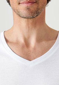 White cotton V-neck t-shirt featuring a ribbed texture. The neckline is well-defined, with visible stitching and a relaxed fit.