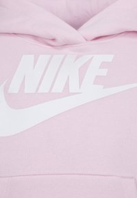 Roze dukserica napravljena od mekog materijala s velikim bijelim "NIKE" logotipom i bijelim swoosh dizajnom otisnutim na prednjoj strani.