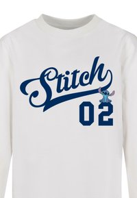 Hvid langærmet t-shirt med et navy blåt "Stitch" grafik og nummeret "02." Inkluderer en tegneseriefigur af Stitch i blå med lyserøde accenter.