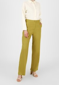 Hellgrüne, hoch-taillierte Hose mit geradem Bein, strukturiertem Stoff und breiten Gürtelschlaufen, kombiniert mit einem cremefarbenen Hemd mit Knöpfen.