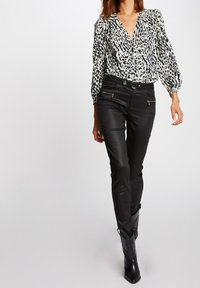 Czarna i biała bluzka w panterkę z bufkami, zestawiona z dopasowanymi czarnymi spodniami z dwoma zamkami błyskawicznymi i eleganckimi czarnymi botkami.