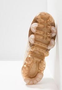 Semelle d'une basket en matériau translucide brun clair avec des picots en caoutchouc ronds, des motifs texturés et une zone de talon renforcée.