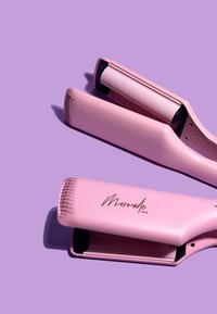 Plancha de pelo de cerámica rosa con acabado brillante, bordes curvados y un agarre texturizado. Presenta el logotipo "Mermade Hair" en escritura metálica.