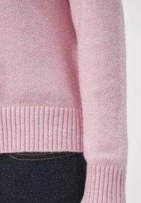 Mjuk rosa tröja med ribbade manchetter och nederkant, med en slät textur och avslappnad passform, i kombination med mörka denim.