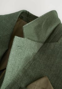 Grüner strukturiert Blazer mit einem markanten Kragen und gestickten Details, versehen mit einem glatten Innenfutter in einem kontrastierenden Farbton.