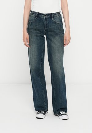 Vide benbukser laget av mørkeblå denim. Kjennetegn inkluderer fem lommer, knappestenging og en subtil falmet struktur. Følger med et par svarte joggesko.