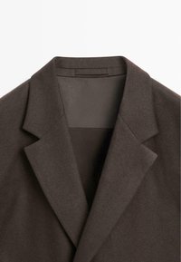 Brązowa marynarka z klapami z wcięciem, charakteryzująca się gładką teksturą i minimalistycznym wzornictwem. Wnętrze podszyte w odcieniu dopełniającym.