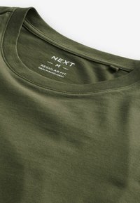 Olíva zöld pamut póló kerek nyakkal, sima textúrával, a "NEXT" felirattal, amely a normál fazont jelzi, Bangladesben készült.