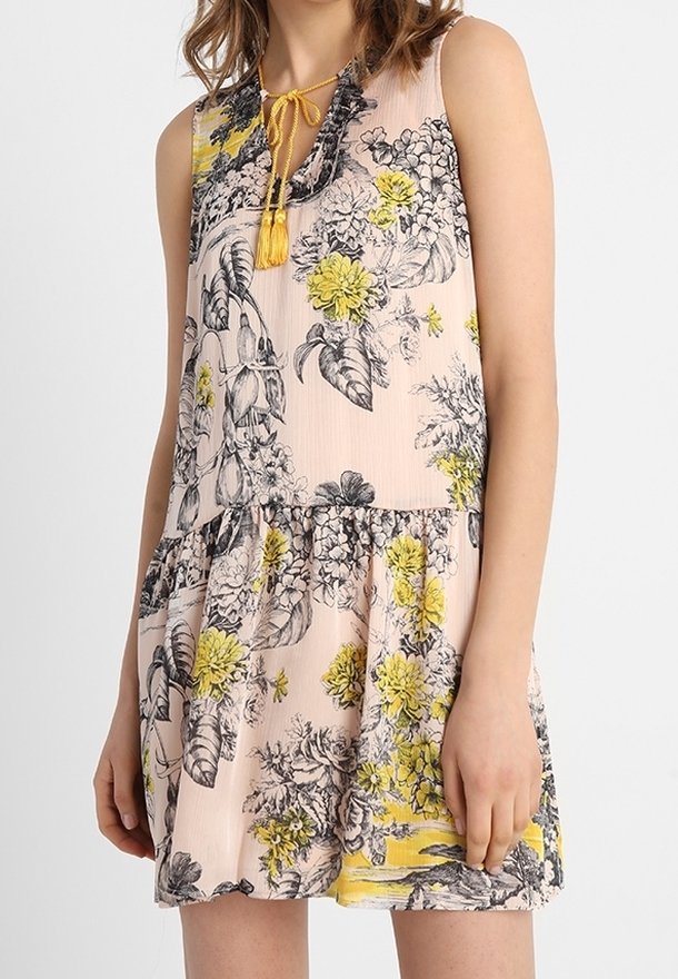 Robe sans manches à motif floral en rose clair, avec des fleurs noires et jaunes, un ourlet en volant à plusieurs niveaux et une fermeture à nouer au cou avec des franges.