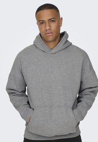 Grauer Kapuzenpullover mit weicher Textur, ausgestattet mit einer Vorderasche und weiten Ärmeln, vor einem hellen Hintergrund.