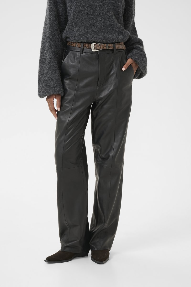Calças largas de couro preto com costuras, combinadas com um cinto castanho estampado e botas de salto castanho-escuro. Suéter cinza suave.