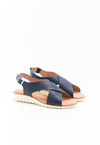 Sandali intrecciati blu navy con cinturini incrociati, soletta imbottita e suola bianca bassa. Include una cinghia alla caviglia regolabile con hardware argento.