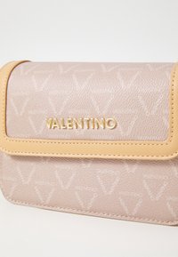 Růžová kožená kabelka s hnědými detaily, zdobená vyraženým logem "Valentino" a vzorovanou texturou, obdélníkového tvaru se zapínáním na klopu.