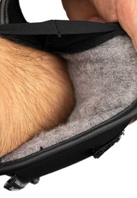 Schwarzes Schuh- oder Stiefelinnere mit weichem grauem Wollfutter, das Textur und gepolsterte Kanten zeigt, in der Hand gehalten mit sichtbarer Haut und Haar.