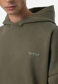 Felpa con cappuccio di colore verde oliva, realizzata in tessuto morbido. Presenta un piccolo logo sul petto e un classico design con tasca a marsupio.