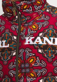 Quilted puffer jacket in vibrant red and multicolored floral pattern, features a high collar, zip closure, and embroidered "KARL" logo.
