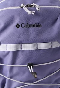 Μωβ υφασμάτινο σακίδιο με λευκές λεπτομέρειες, με κορδόνι στο πάνω μέρος, ελαστικό κορδόνι κλεισίματος και το λογότυπο της Columbia να εμφανίζεται καθαρά.